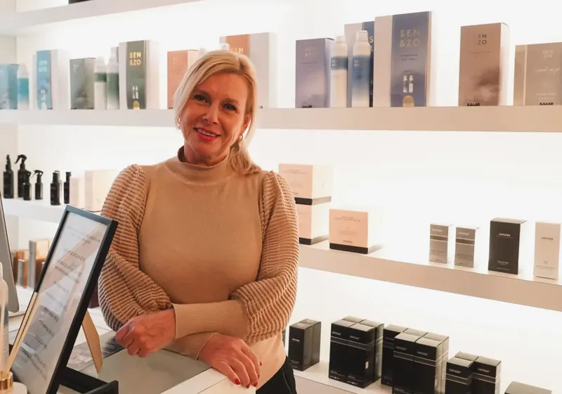 Francien Rongen aan de balie van beautysalon Senssis, voor de verlichte schappen met producten