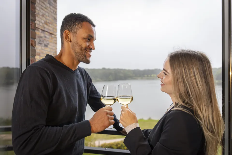 A couple raising a glass of white wine by the window at Parkhotel Horst