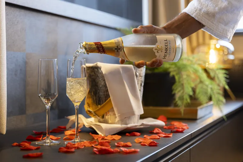 Bubbles being poured into two glasses, with rose petals on the table