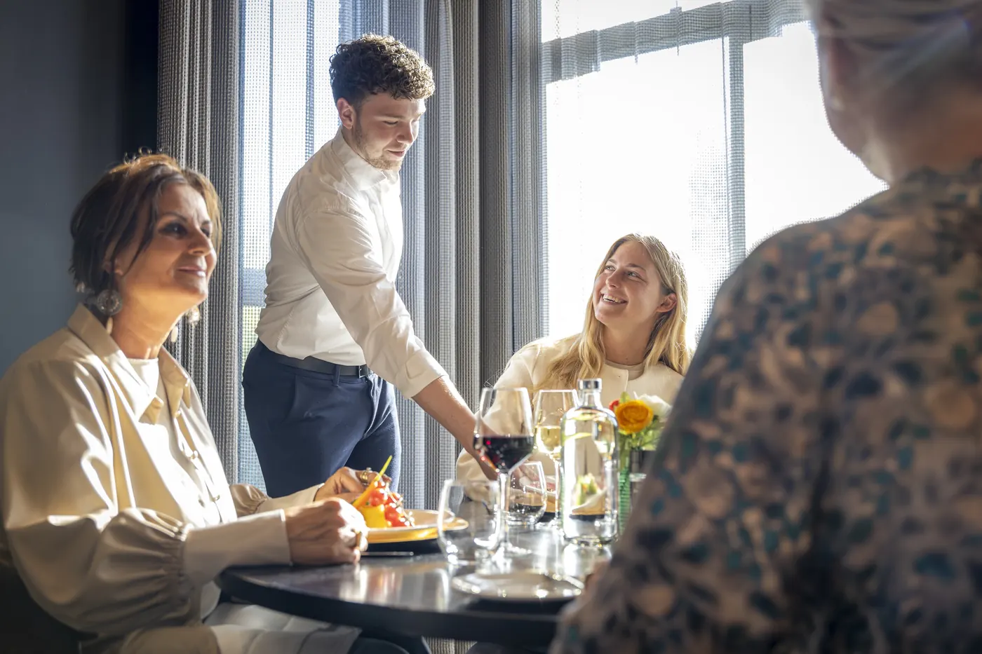 A member of staff pours red wine at the table for guests in restaurant BØFF