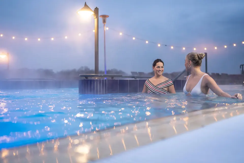 Twee gasten in het warme buitenbad van Thermaalbad Arcen bij schemering