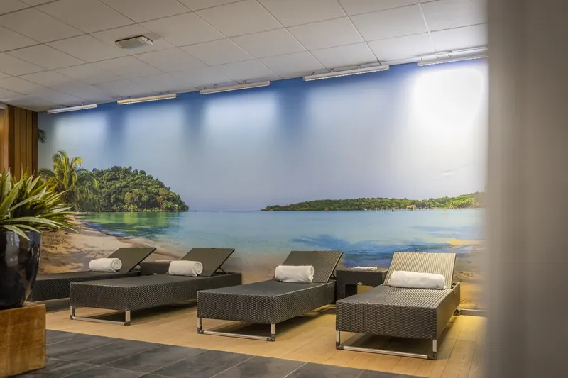 The wellness lounge with loungers in front of a tropical mural