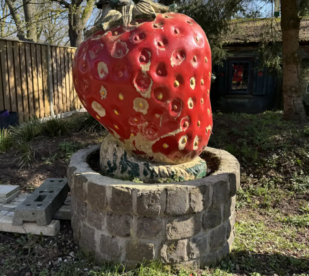 Een grote aardbei als beeld op een stenen sokkel in de tuin van Het Aardbeienland