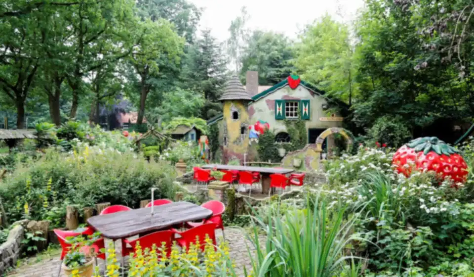 De tuin van Het Aardbeienland met terras, rode stoelen, een sprookjeshuis en de grote aardbei