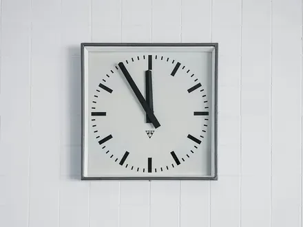 Quadratische Wanduhr an einer weißen Fliesenwand