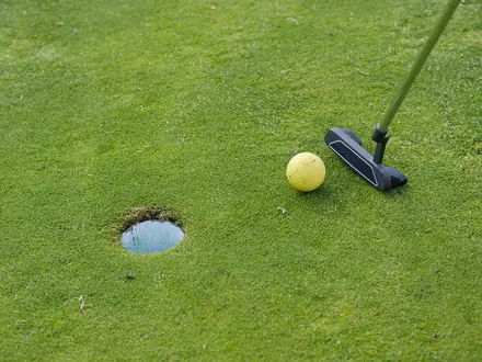 Putter und Golfball nahe am Loch auf dem Grün