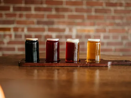 Proefplankje met vier glazen bier, van donker tot blond, voor een bakstenen muur