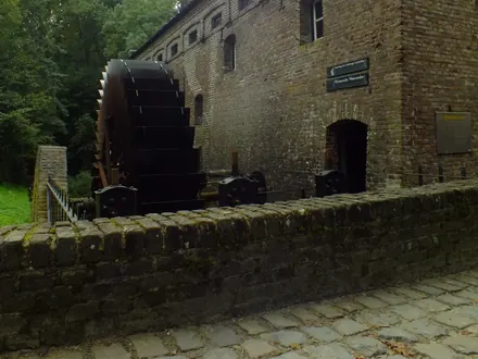Die Wassermühle mit dem großen Wasserrad an der Kopfsteinpflasterstraße