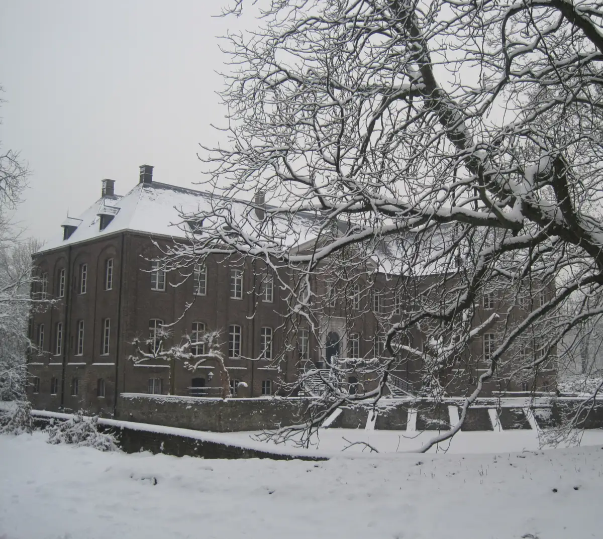 Schloss Arcen im Schnee, durch verschneite Zweige über den Graben gesehen