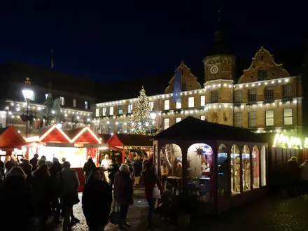 Weihnachtsmarkt vor dem beleuchteten Rathaus von Düsseldorf mit Buden und Weihnachtsbaum