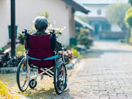 Frau im Rollstuhl auf einem Klinkerweg zwischen Häusern