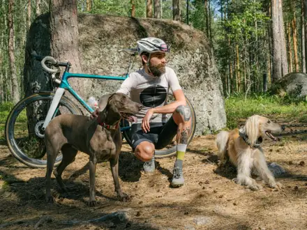 Radfahrer, der mit seinen zwei Hunden auf einem Sandweg im Wald rastet