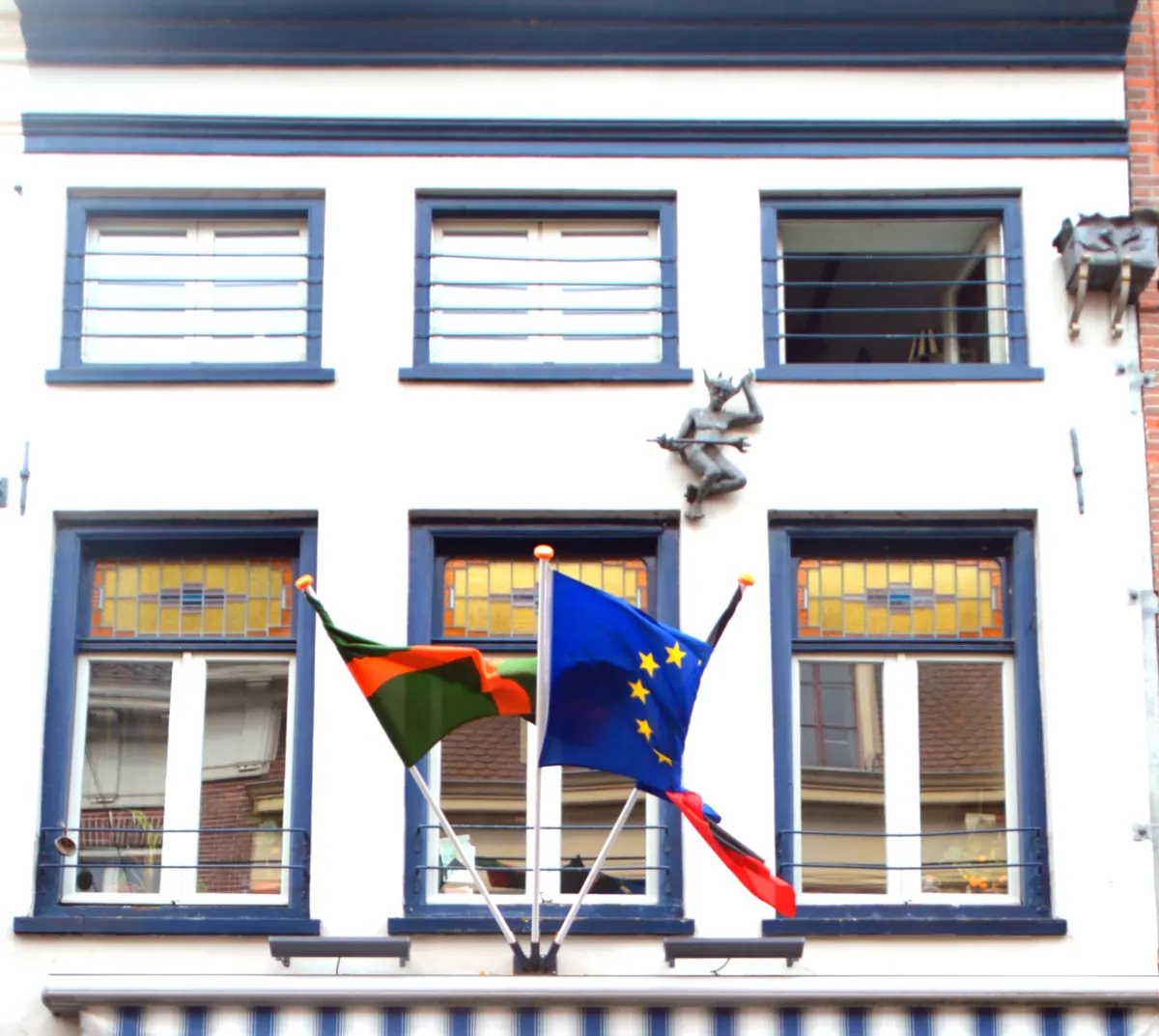 Der obere Giebel von Lange Hezelstraat 59 in Nijmegen, ein Rijksmonument mit Bleiglas über den Fenstern und einem kleinen Teufel an der Fassade