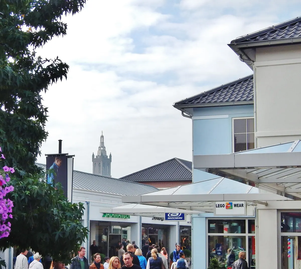 Geschäfte im Designer Outlet Roermond mit dem Turm der Christoffelkathedraal im Hintergrund