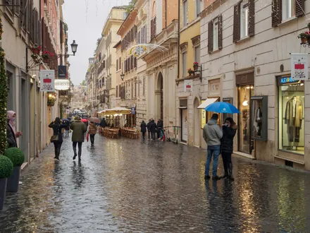 Ladenstraße im Regen mit Passanten unter einem Regenschirm