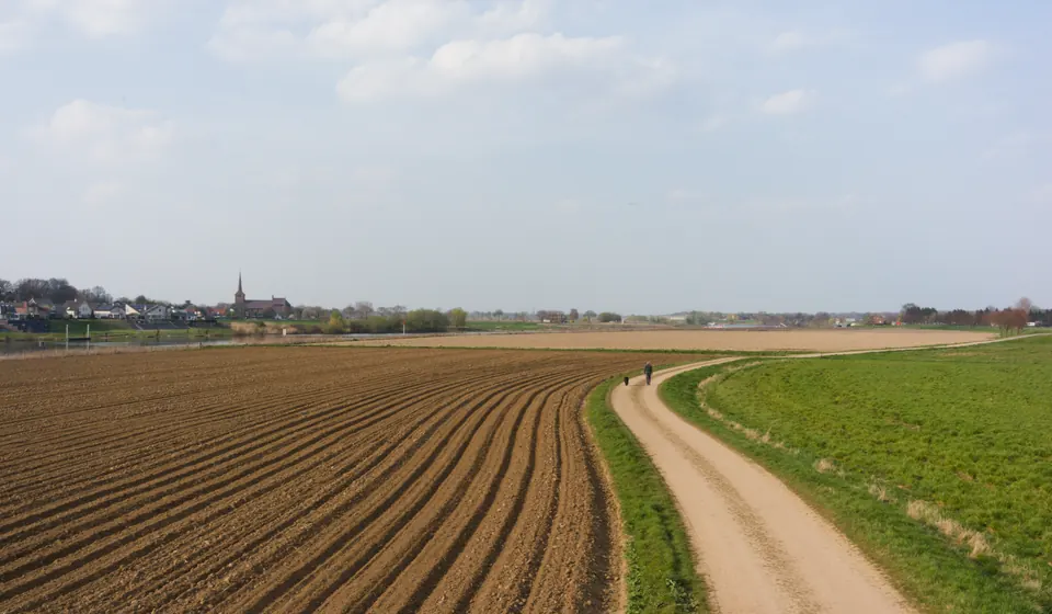 The Pieterpad as a sandy path along the Maas near Velden, with a walker in the distance