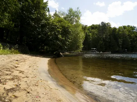 Kleiner Sandstrand an einem klaren See mit Wald am Ufer