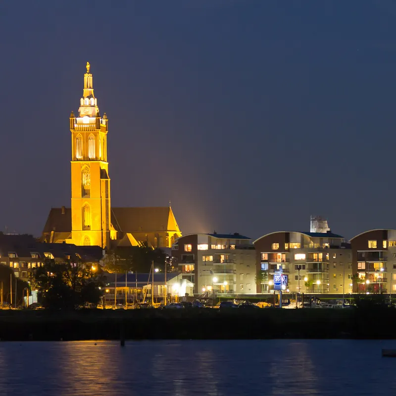 Der beleuchtete Turm der Sint-Christoffelkathedraal in Roermond am Abend, vom Wasser aus gesehen