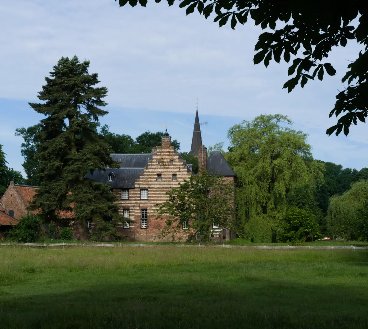 Kasteel De Borggraaf in Lottum mit Treppengiebel, von der Maas aus gesehen, mit dem Kirchturm dahinter