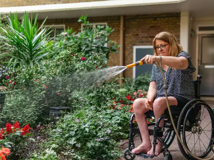 Frau im Rollstuhl gießt blühende Pflanzen in einem Garten