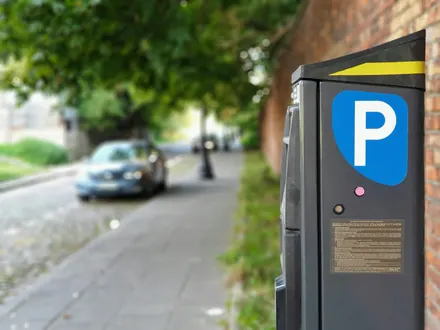 Parkscheinautomat mit blauem P an einer Straße mit Bäumen