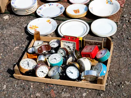 Holzkiste mit alten Weckern und Tellern auf einem Flohmarkt