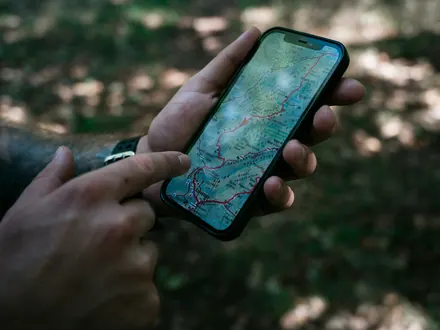 Hände mit einem Handy, auf dem eine Wanderkarte geöffnet ist
