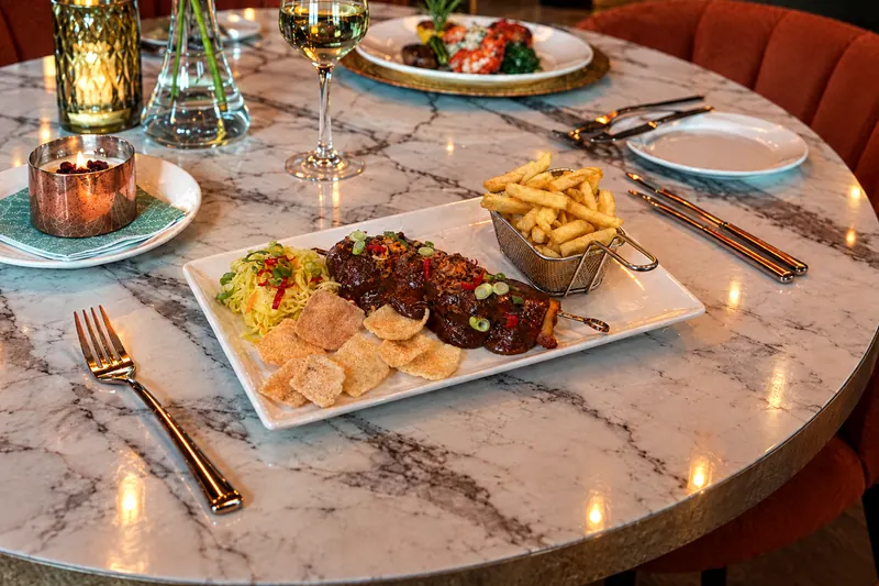 Chicken satay from restaurant BØFF: skewer of marinated chicken thigh with satay sauce, atjar, cassava crackers and fries on the marble table