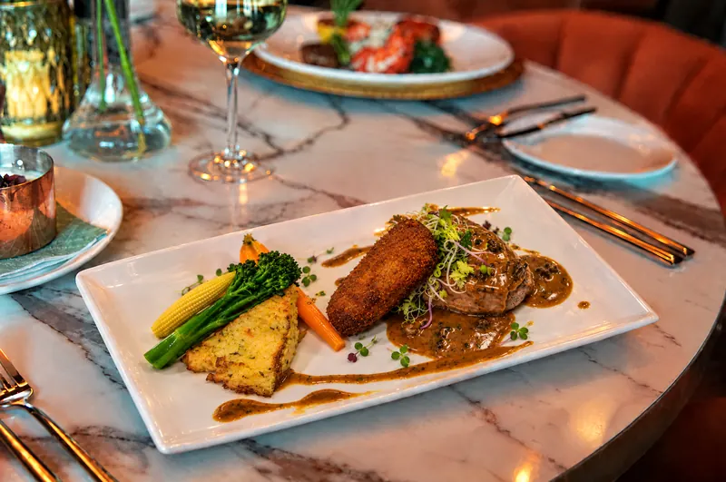 Veal escalope from restaurant BØFF: veal escalope with a homemade veal croquette, potato rösti, caramelised shallot and morel sauce on a white plate on the marble table