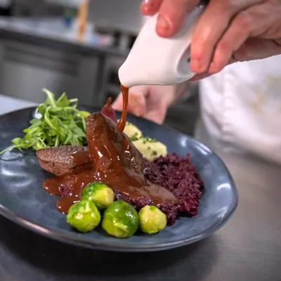 Kok giet saus over een hoofdgerecht in de keuken van restaurant BØFF
