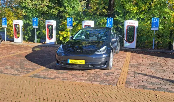 Een Tesla aan de Supercharger op de parkeerplaats van Parkhotel Horst