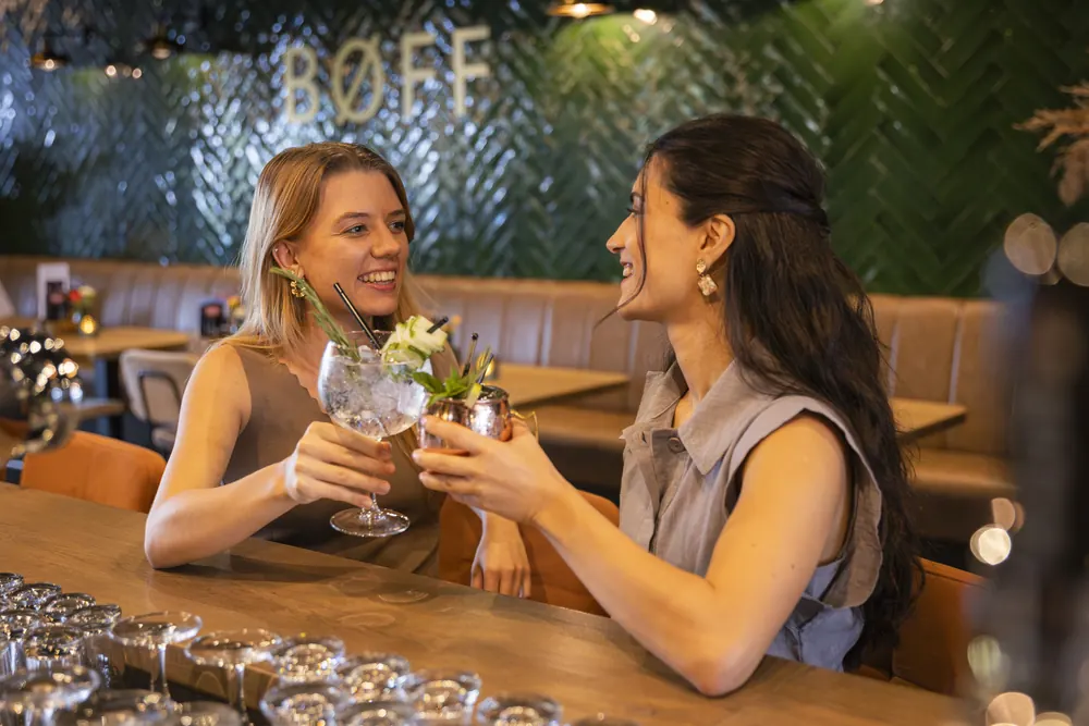 Two friends raising their cocktails at the BØFF bar