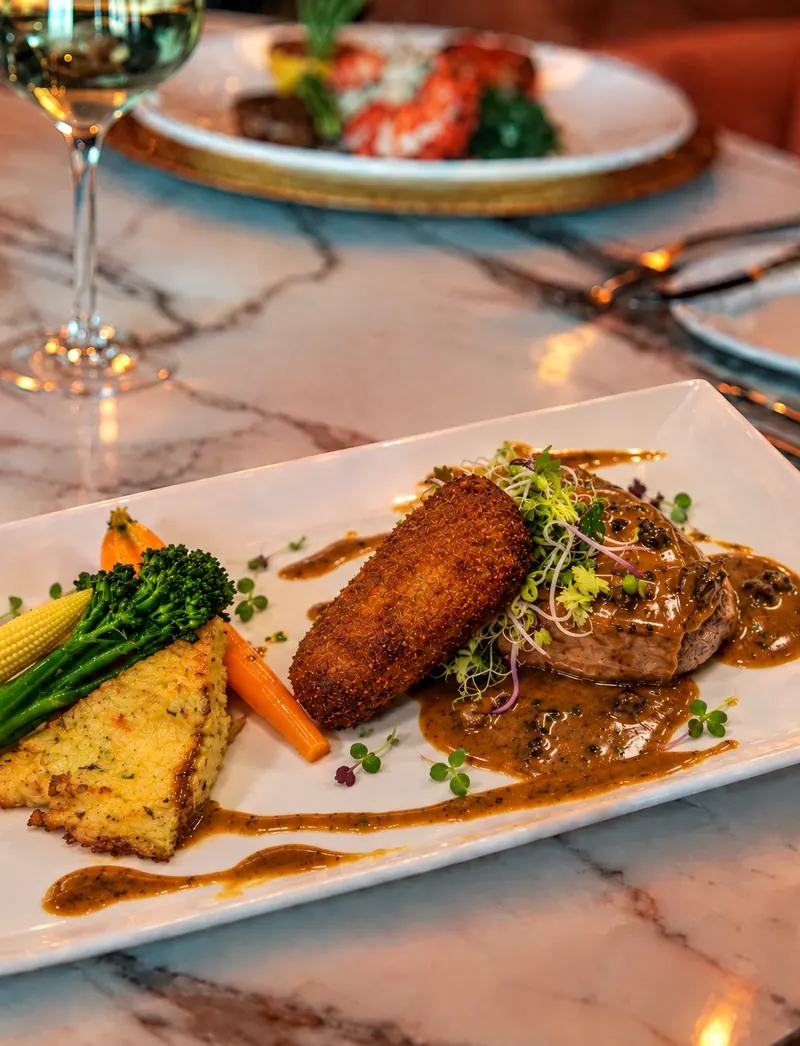 Veal escalope from restaurant BØFF: veal escalope with homemade veal croquette, potato rösti, caramelised shallot and morel sauce on a white plate on the marble table