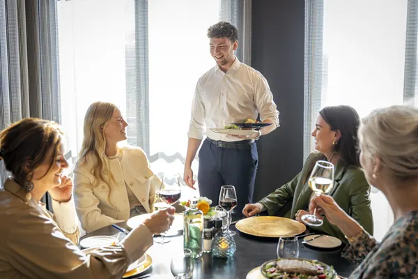 The waiter serves a plate to four friends with a glass of wine