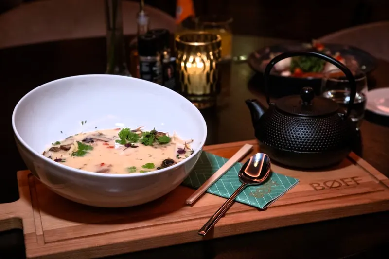 A bowl of soup with fresh herbs on a BØFF wooden board, by candlelight