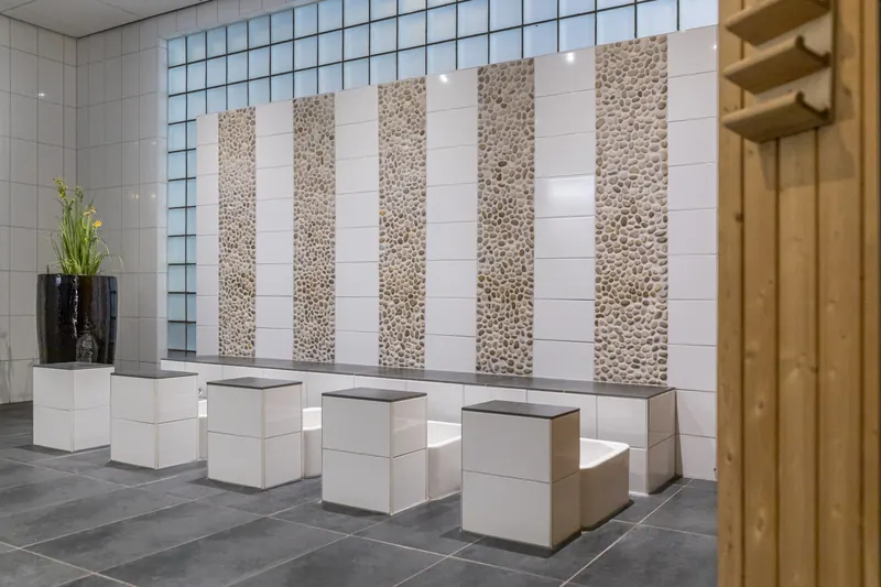 De betegelde spa-hal met kiezelwand en houten saunadeur
